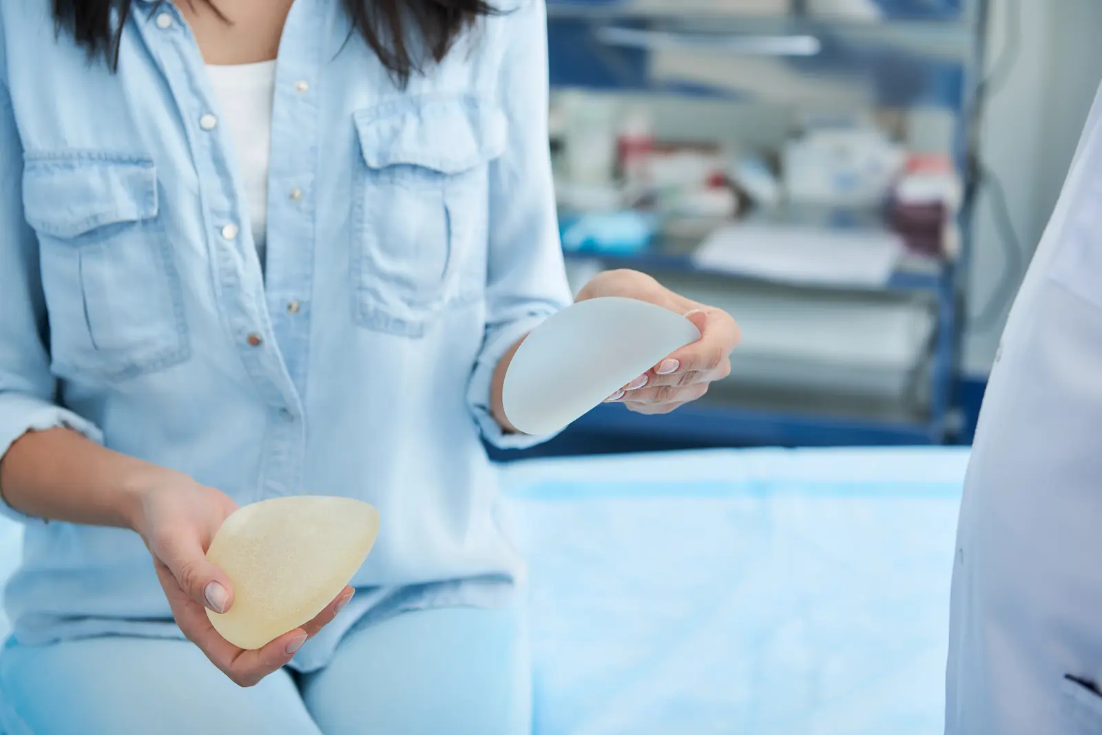 Woman holding two breast implant options in a medical office.